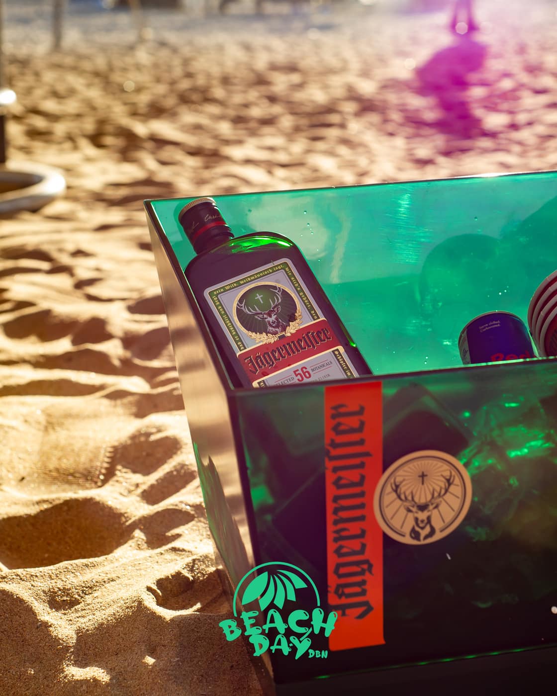 An ice bucket of drinks on the sand in late afternoon light